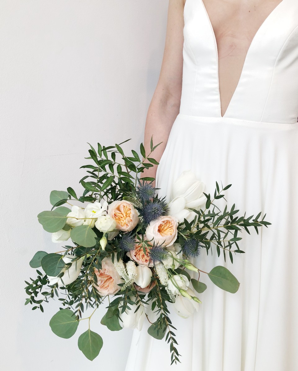 Canadian bridal label Aesling. Image features a close up of the Orenda dress with deep neckline and a gorgeous peach and cream floral bouquet with eucalyptus